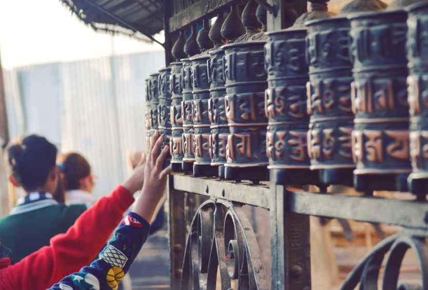 unrecognizable pilgrims touching prayer wheels in ancient temple in nepal