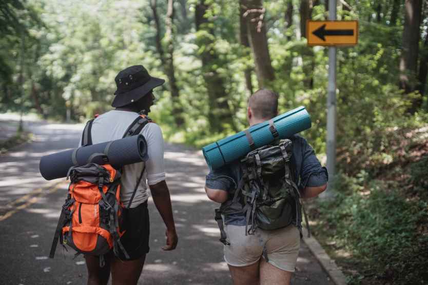 unrecognizable diverse male hikers with backpacks walking along road
